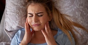 Woman with sleep apnea in Richardson, TX rubbing sore jaw